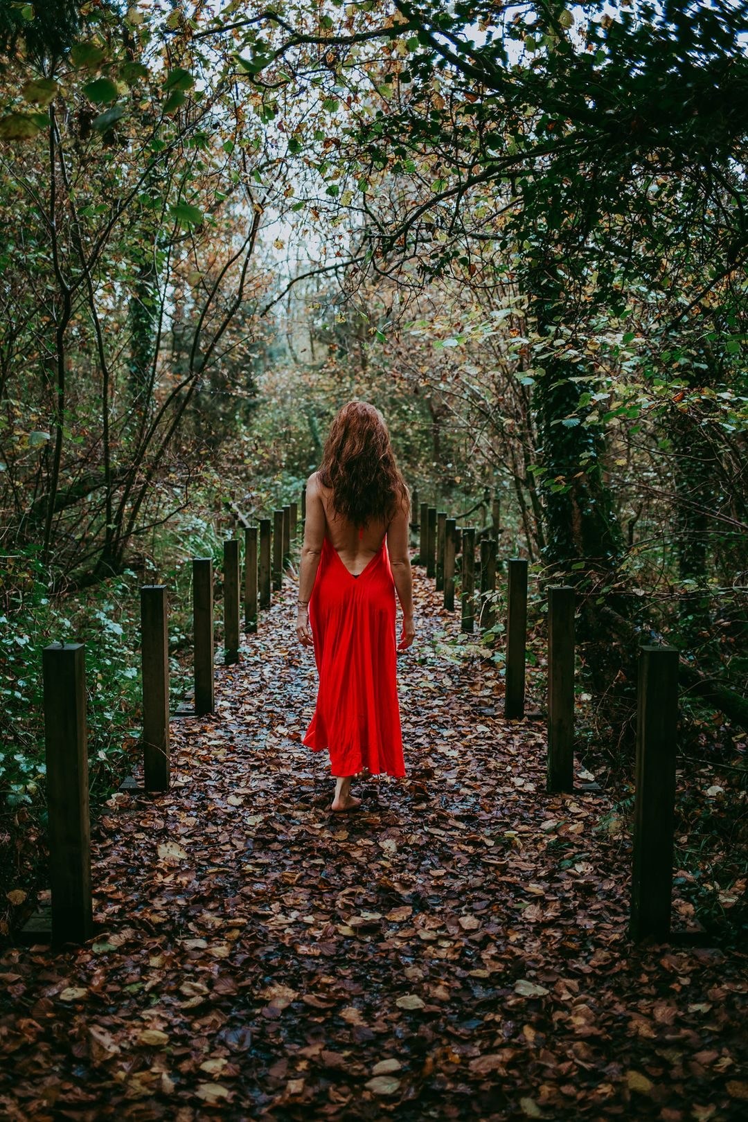 A woman in a red dress walking a wooded path